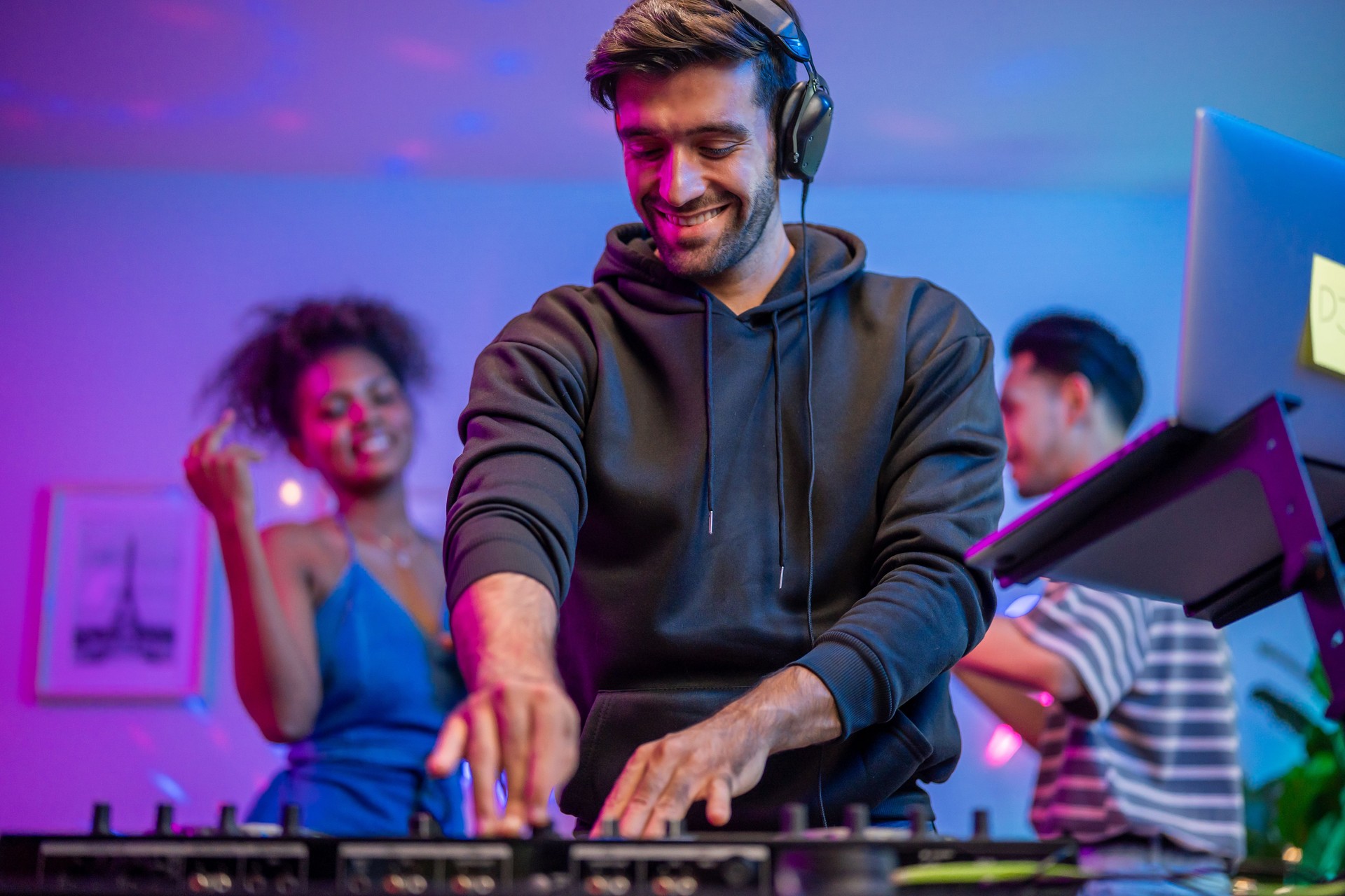 Group of diverse man and woman dancing with DJ mixing music on console. Attractive young teenager friends having fun with DJ mixing and scratching music mixer controller at house party with neon light